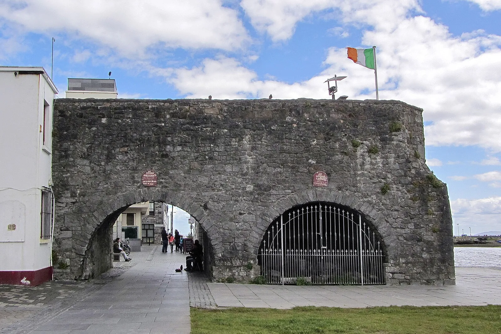 The Spanish Arch in Galway, a weathered stone arch in the old city wall beside the river, with an Irish flag flying above it