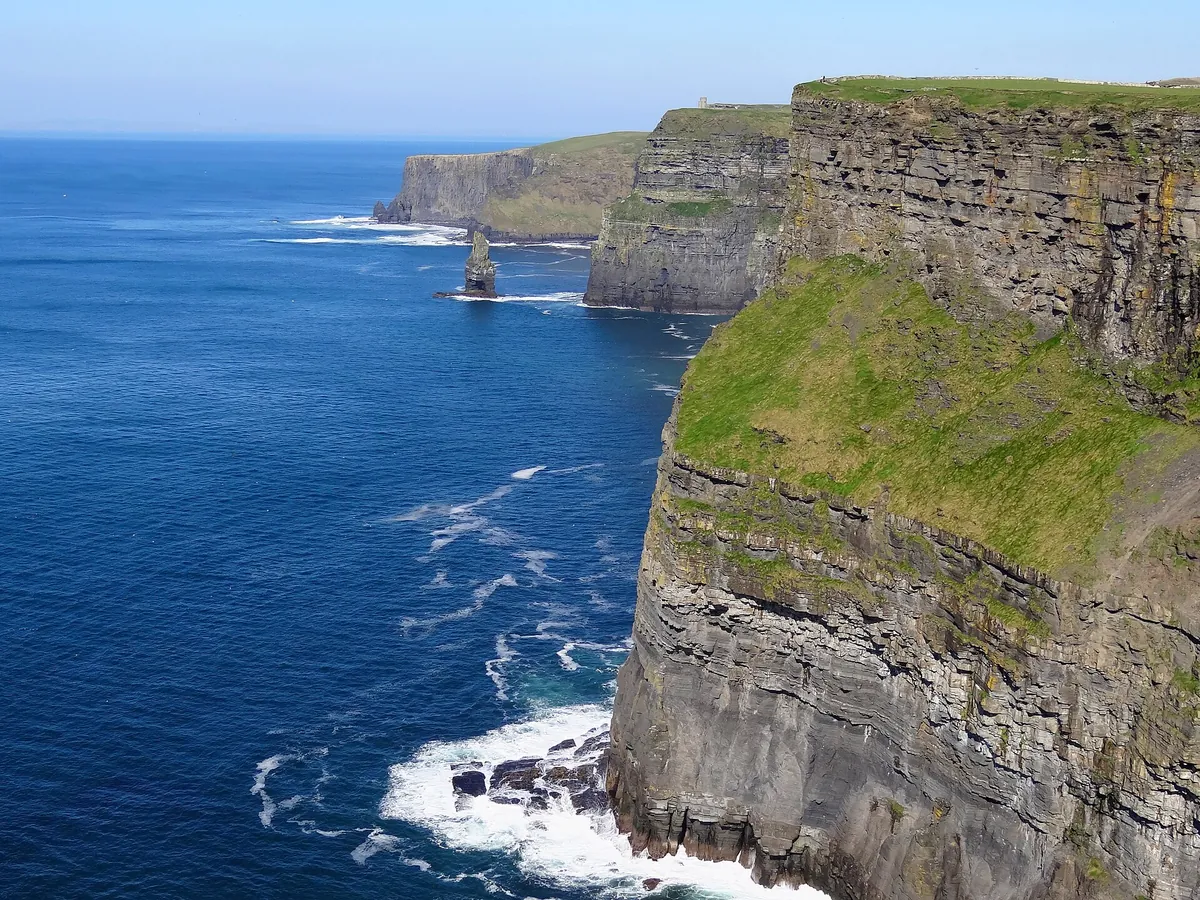 The Cliffs of Moher seen from the south, with O'Brien's Tower on the cliff top and the Atlantic below under a blue sky
