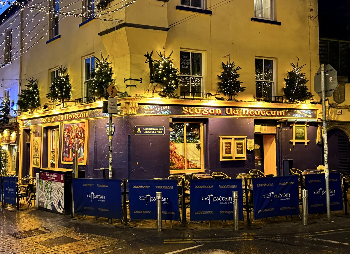A yellow corner pub on Quay Street in Galway, lit up at night with small Christmas trees on its first-floor ledge