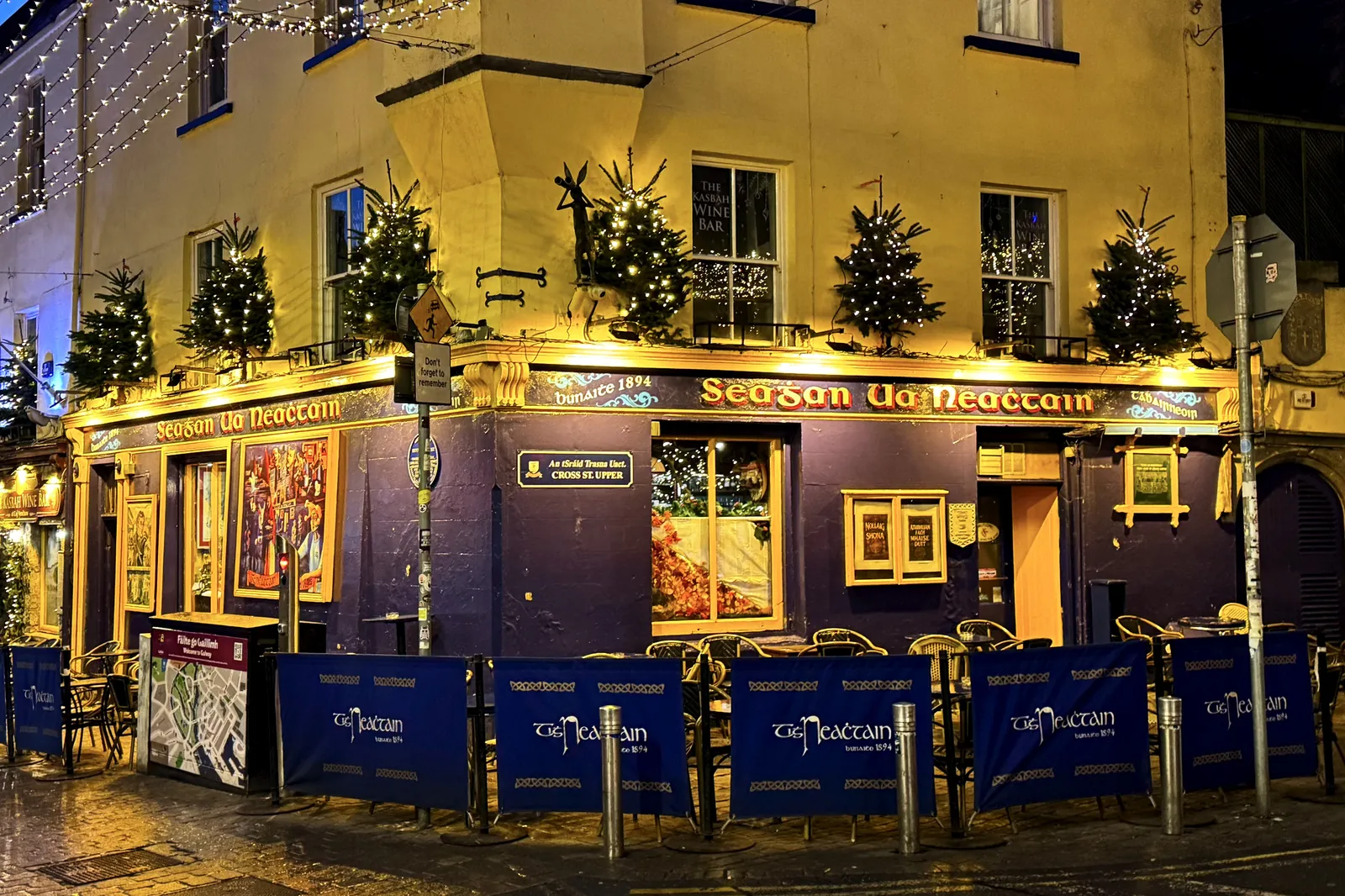 A yellow corner pub on Quay Street in Galway, lit up at night with small Christmas trees on its first-floor ledge